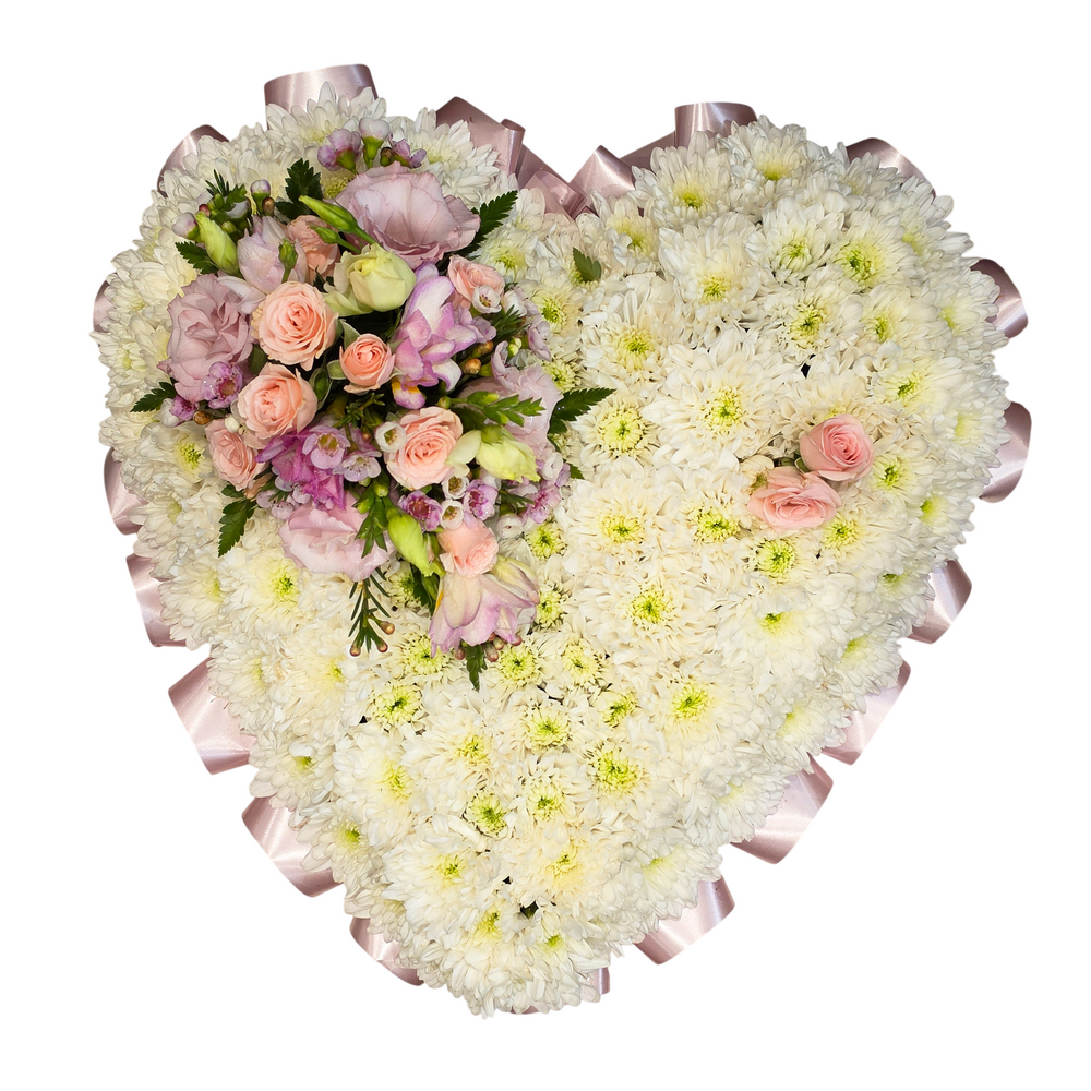 A heart-shaped floral arrangement featuring a large bed of white chrysanthemums with a cluster of pink roses and light purple lisianthus blossoms, finished with pale pink ribbons.